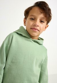 Felpa con cappuccio verde chiaro realizzata in cotone morbido. Presenta una vestibilità comoda, tasca a marsupio e maniche ampie e confortevoli.