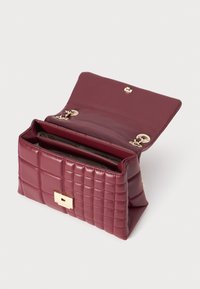 Sac à main matelassé bourgogne avec une texture en cuir lisse, des accessoires en métal doré et une fermeture à rabat sécurisée avec un fermoir rectangulaire.