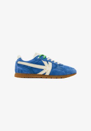 Zapatilla de deporte de ante azul con diseño blanco de la Union Jack, cordones verdes y blancos, y suela de goma, vista de lado.