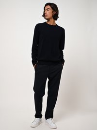 Marineblauer Strickpullover mit rundem Ausschnitt, kombiniert mit dunklen Hosen und weißen Sneakern. Schlichtes Design und weiche Textur.
