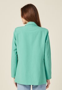 Blazer verde menta con colletto a punta, maniche lunghe e design senza cuciture. Realizzato in tessuto leggero, presenta una superficie liscia.