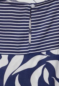 Marinblå och vitrandig tyg upptill med knappstängning; blommönster i marinblått och vitt nertill; slät yta.