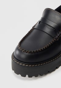 Schwarze Lederloafers mit einer dicken Gummisohle. Verfügt über dekorative Nähte in Hellbraun und ein geformtes Design auf der Oberseite.