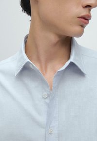 Jasnoniebieska koszula z guzikami, wykonana z teksturowanej tkaniny, z klasycznym kołnierzykiem, małymi guzikami oraz dopasowanym krojem wokół szyi.