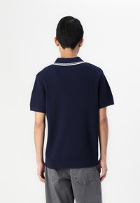 Tricou polo bleumarin cu un design texturat, având un guler clasic și două dungi albe. Mâneci scurte și o margine dreaptă completează aspectul.