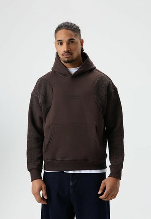 Bruine hoodie met een gestructureerd ontwerp op de mouwen, een grote voorkantzak en een capuchon met trekkoord. Heeft de tekst "BYE BYE LOSER" op de voorkant.