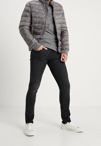 Grå puffjacka med horisontell sömnad, dragkedja och ribbade muddar. Lager på lager grå t-shirt, svarta skinny jeans och vita sneakers.