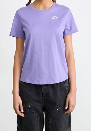 Personne portant un T-shirt Nike violet clair à manches courtes et un pantalon noir ample avec des poches avant visibles et des coutures.