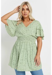 Light green floral top with a V-neck, short ruffled sleeves, and a smocked waist. Flowy design with small white and yellow flower patterns.