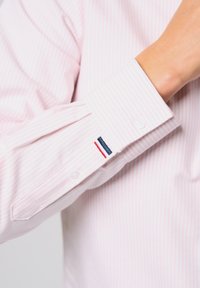 Gestreepte roze overhemd met knoopmanchet, voorzien van een klein geborduurd logo in marineblauw en wit. Zacht stof met een gladde textuur.