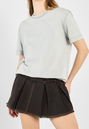 T-shirt en coton gris clair accompagné d'une jupe plissée en jean noir avec ourlet effiloché et surpiqûres contrastantes.