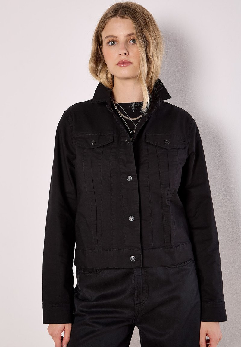 Czarna kurtka jeansowa z zapięciem na guziki, dwoma kieszeniami na piersi i usztywnionym kołnierzem. Posiada pionowe przeszycia i krótki krój.