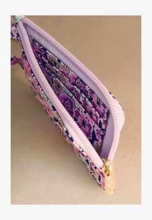 Kis textil tasak lila virágmintával, világos rózsaszín cipzárral és arany cipzárhúzóval, részben nyitva, hogy látható legyen a belső textil bélés.