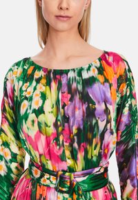 Bunt bedrucktes Blumenkleid mit weitem Ausschnitt, langen Ärmeln und einem Stoffgürtel in der Taille. Hergestellt aus leichtem, fließendem Material.