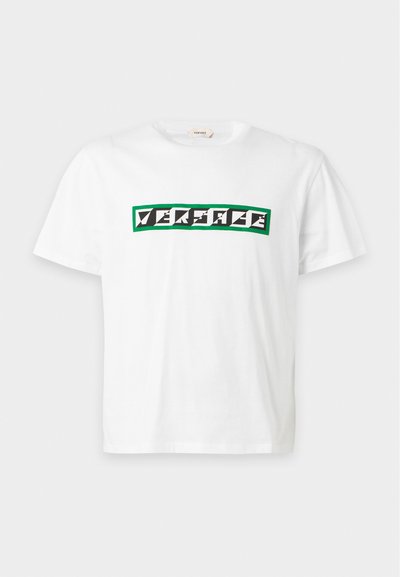 T-shirt blanc à manches courtes avec logo géométrique noir et blanc Versace à l'intérieur d'un cadre rectangulaire vert sur la poitrine.