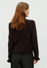 Sötétbarna kötött pulóver texturált felülettel, fecske aljjal és fodros mandzsettával. A hátulról készült nézet lazán illeszkedő fazont és hosszú ujjakat mutat.