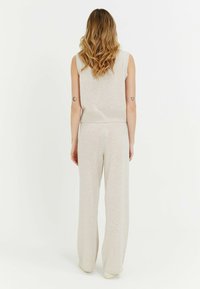Ensemble tricoté beige clair à deux pièces avec top sans manches et pantalon évasé, présentant une texture douce et des bords en côtes.