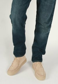 Scarpe in suede beige con una texture liscia, punta rotonda e design con lacci, abbinate a jeans in denim blu scuro.