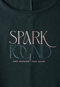 Tmavě zelená mikina s textem "SPARK FOUND" v různých písmenech; další text níže zn�í "KEEP GROWING KEEP GOING" bílou barvou.