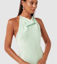 Mint green halter neck dress with draped front, made from soft fabric. Model wearing silver hoop earrings, smooth skin texture.