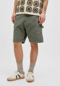 Khaki grønne shorts i bomulds-twill, med sidelommer og en afslappet pasform, parret med beige ribbede sokker og retro-stil sneakers.
