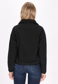 Juodas švarkas su apykakle, lygia tekstūra ir raglan tipo rankovėmis, derinamas su tamsiomis džinsomis. Nugarinė dalis turi paprastą dizainą be dekoracijų.