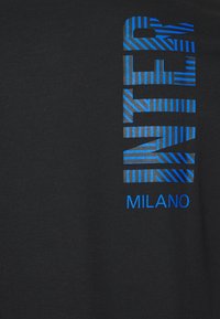 Čierne bavlnené tričko s odvážnym modrým prúžkovaným textom "MILANO", s rôznymi vzormi a hrúbkami čiar na hornej polovici.