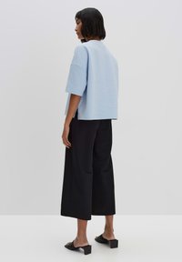 Lichtblauwe, met textuur, oversized top met korte mouwen, gecombineerd met zwarte wijde broek en zwarte sandalen met blokhak.