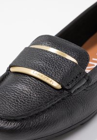 Mocassin en cuir noir avec dessus texturé, barre d'accent dorée et détail embossé « Calvin Klein » sur la bride. Doublure intérieure lisse.