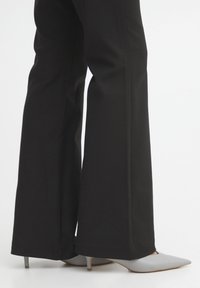 Pantaloni neri a gamba larga con una texture liscia, caratterizzati da un design pulito. Abbinati a tacchi grigi a punta con tacco sottile.
