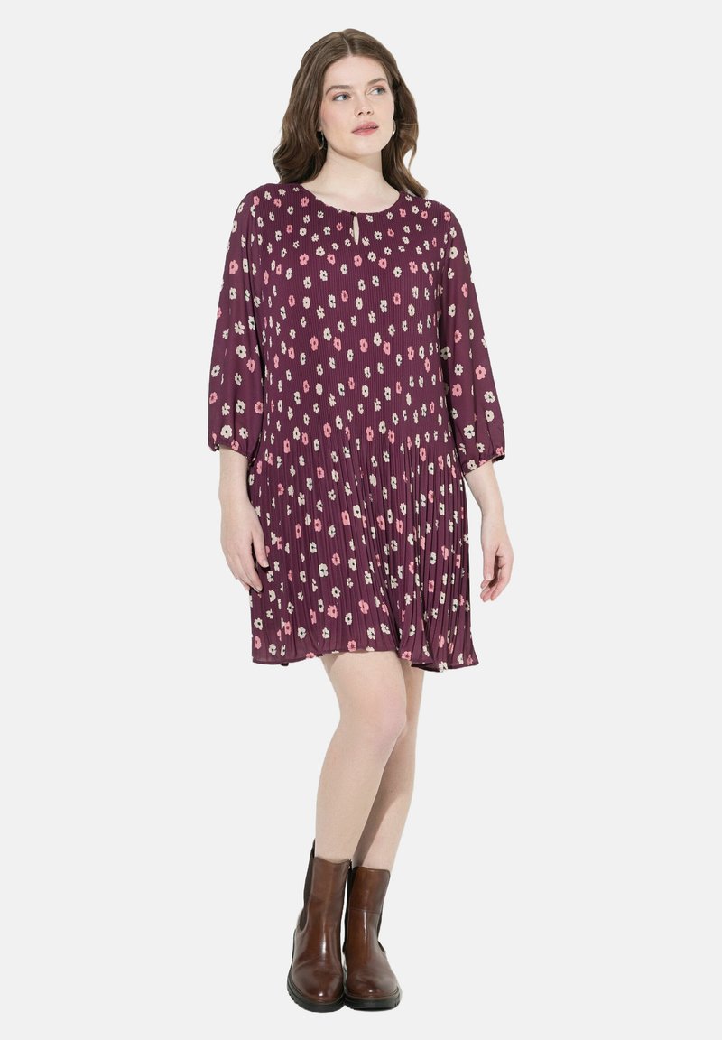 Lila Blumenkleid mit dreiviertel Ärmeln, gefältelter Textur, Rundhalsausschnitt und Oberschenkellänge, kombiniert mit braunen Stiefeletten.