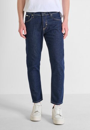 Dark blue denim jeans with a straight cut, subtle stitching, and five-pocket design, paired with white low-top sneakers.