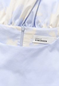 Vaaleansininen kangas, jossa on pehmeä rakenne; sisältää vetoketjukiinnityksen ja "KAREN BY SIMONSEN" -merkin. Sisällä on hienovarainen pilvikuvio.