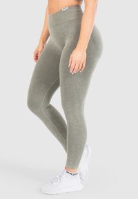Leggings verde oliva a vita alta con vita a coste e texture sottile. Abbinati a sneakers bianche con dettagli neri.