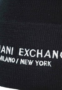 Gorro de punto negro con texto bordado en blanco que dice "Milán / Nueva York." La textura es suave y tiene un diseño acanalado.