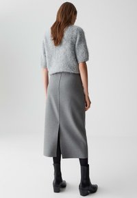 Grauer flauschiger Pullover mit kurzen Ärmeln, kombiniert mit einem langen, eng anliegenden grauen Rock mit einem Schlitz hinten, getragen mit schwarzen Knöchelboots.