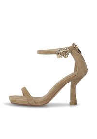 Sandale à talon haute beige avec une finition en daim. Présente une fine bande autour de la cheville, une large bande au niveau des orteils et des accents décoratifs en strass.