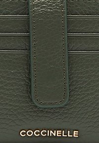 Portefeuille en cuir vert avec une surface texturée, des rayures verticales, une fermeture à rabat et un logo doré en bas.