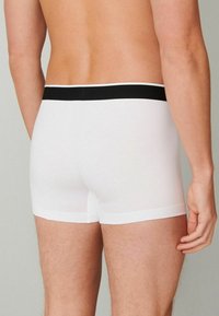 White cotton boxer briefs with a black elastic waistband, featuring a smooth texture and fitted design, shown from the back.