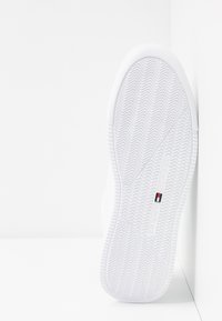 Weißer Sneaker mit einer strukturierten Gummisohle, die ein Zickzack-Muster zeigt, sowie subtiler Markierung in Rot, Weiß und Blau an der Seite.