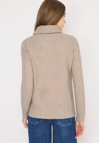Beżowy sweter z dzianiny z kołnierzem na złożeniu, długimi rękawami i prążkowanym wykończeniem. Posiada fakturowany wzór i luźny krój.