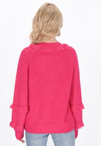 Maglione rosa fuzzy lavorato a maglia con un colletto frangiato e accenti sulle maniche. Taglio loose con una texture a coste, abbinato a jeans blu.