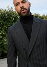 Blazer de color gris carbón de doble botonadura con finas rayas, solapas con muesca y un pañuelo de bolsillo, combinado con un cuello de tortuga negro.