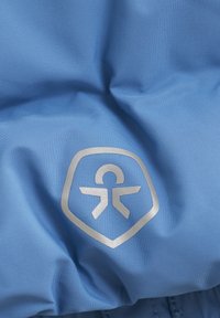 Helles blaues Gewebe mit glatter Textur, das ein silbernes Schildlogo mit einer Personenikone und stilisierten Armen zeigt.