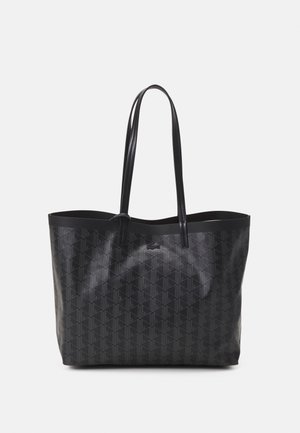 Bolso tote negro con asas largas, patrón geométrico y pequeño logo de cocodrilo en el frente, sobre un fondo blanco liso.