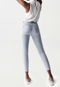 Jeans skinny de color gris claro con cintura alta, bolsillos traseros y un diseño ajustado, acompañados de una blusa blanca y tacones blancos con tiras.