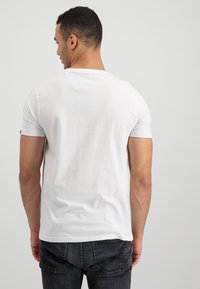 Bílé tričko s krátkým rukávem z bavlny, s přiléhavým střihem a kulatým výstřihem. Pohled zezadu ukazuje minimalistický styl bez viditelných log.