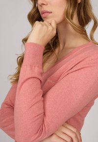 Pull léger rose à col en V avec manches longues, fabriqué à partir de matériaux doux, présentant de subtils détails de couture le long du col et des poignets.