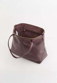 Burgundowa skórzana torba tote z złotym suwakiem, pojedynczym paskiem na ramię i wewnętrzną kieszenią na zamek. Gładka tekstura i zorganizowany design.