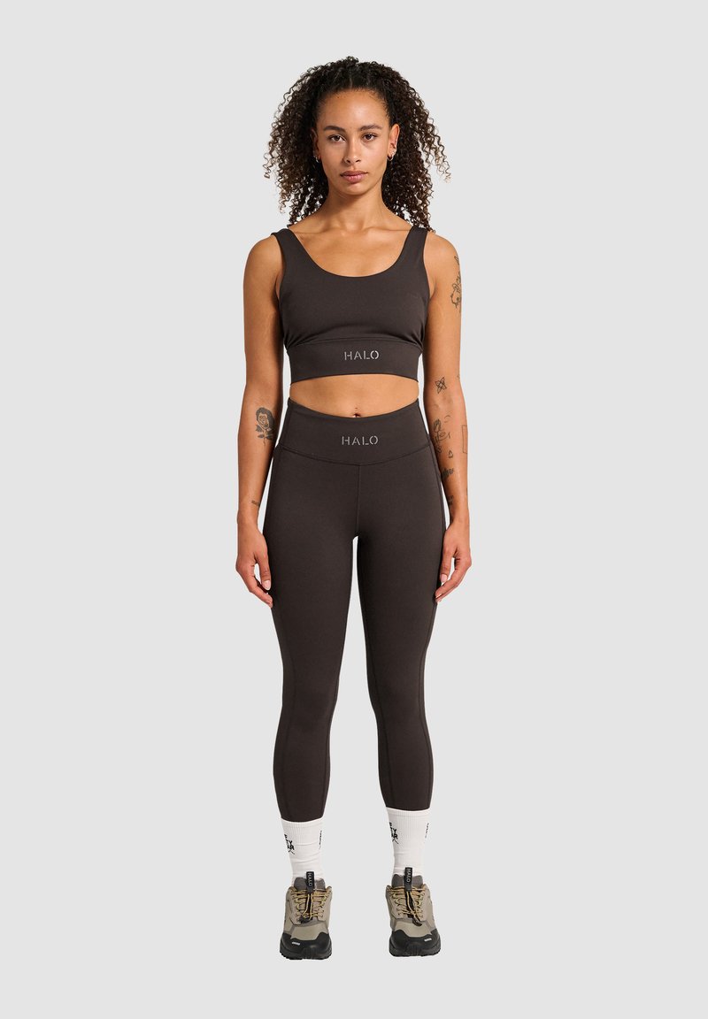 Brun kort topp och högmidjade leggings i stretchigt material. Logotyper visas på båda plaggen. Modell med vandringskängor och strumpor.